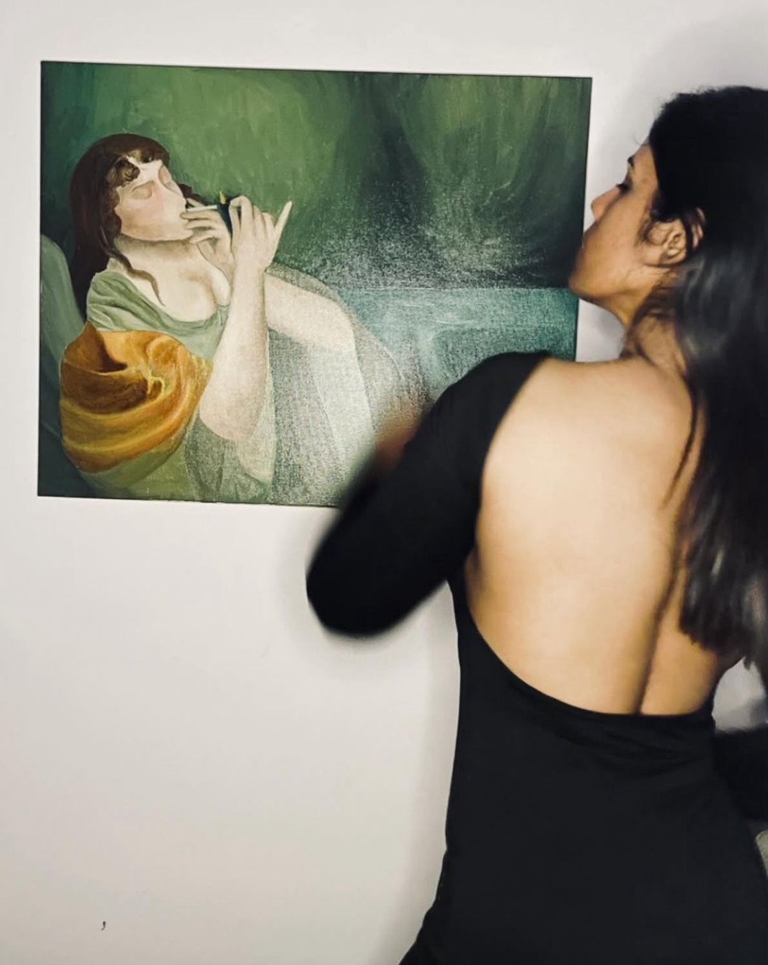 Praksha standing beside her green painting of a woman lighting a cigarette